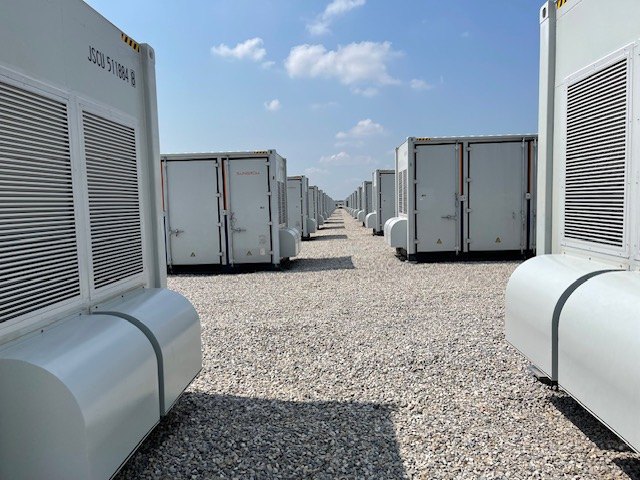 Rows of utility-scale battery storage enclosures receding to the horizon.
